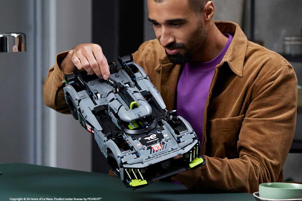 A young man looking at a LEGO® Technic PEUGEOT 9X8 24H Le Mans Hybrid Hypercar.