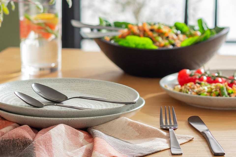 Stainless steel cutlery and tableware set on a dining room table.
