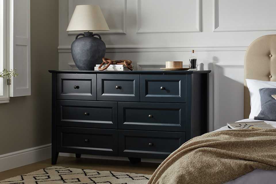 Wooden chest of drawers in black against a panelled wall.