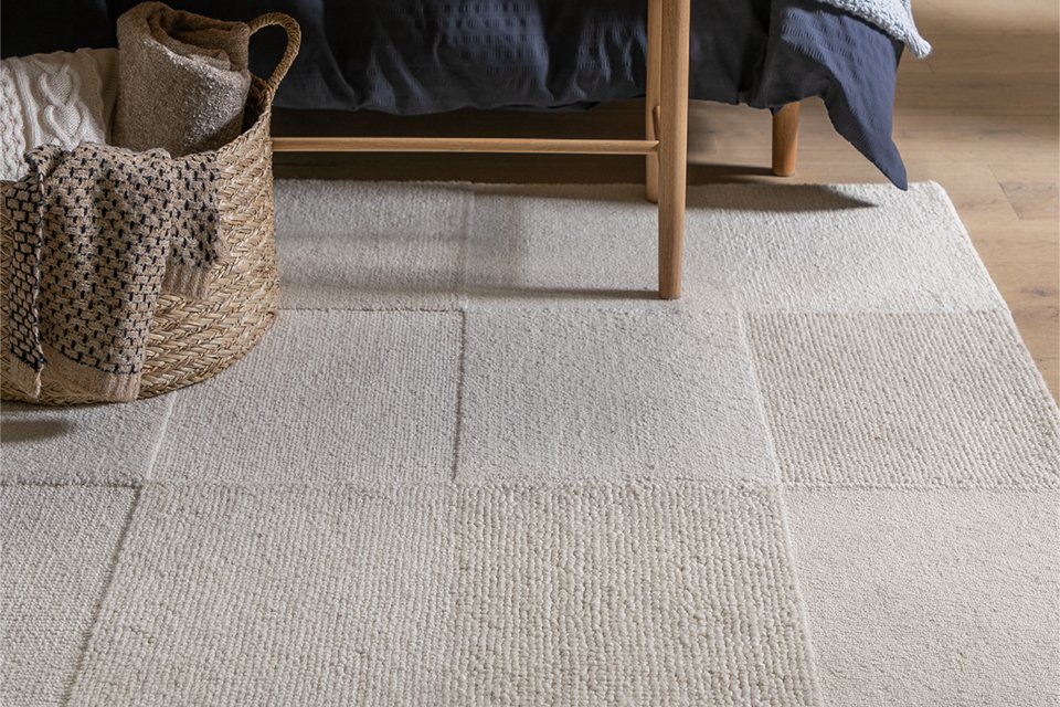 Habitat Checkerboard rug in neutral tones, placed in a bright, modern living room. The wool rug features a bold high-low checkerboard pattern with a soft cut pile texture, adding warmth and visual interest to the wooden floor.
