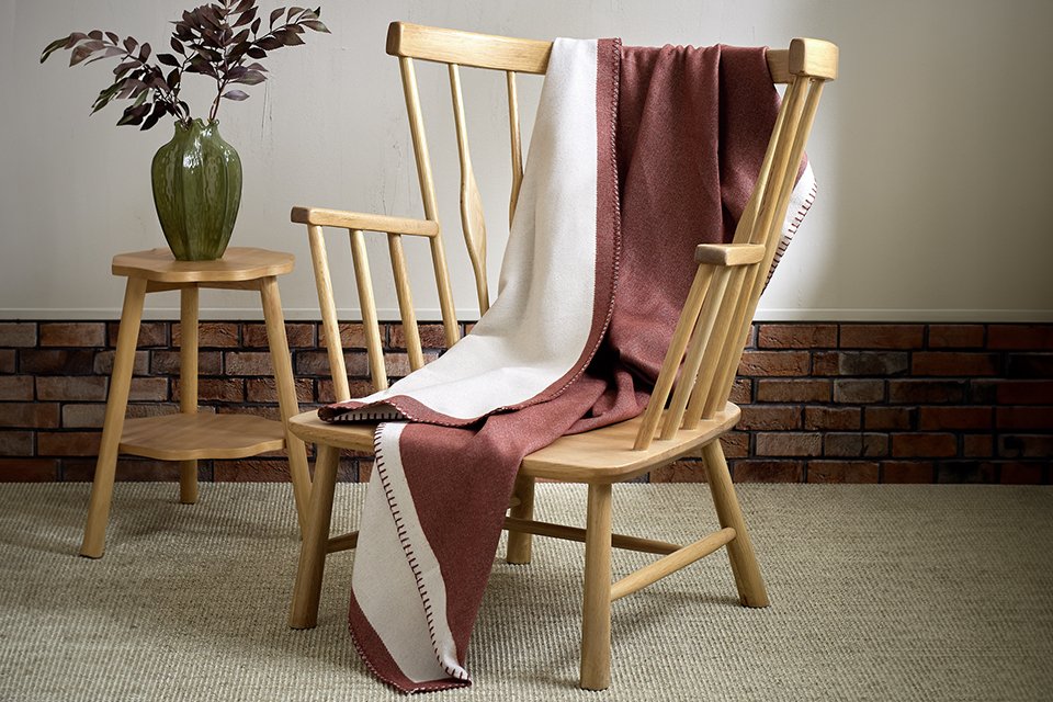 Blush pink throw draped over a wooden armchair, showcasing its soft texture and cosy appearance in a modern living room setting.