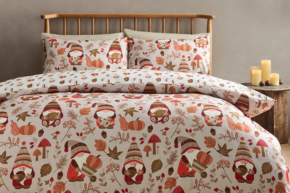 Autumn-themed bedding set with gnome, pumpkin, and leaf print on a neatly made bed with a wooden headboard.