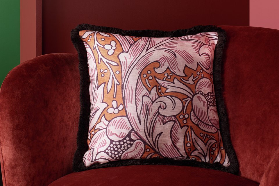 Colurful floral print square cushion with red frayed edge in front of matching floral print curtain.