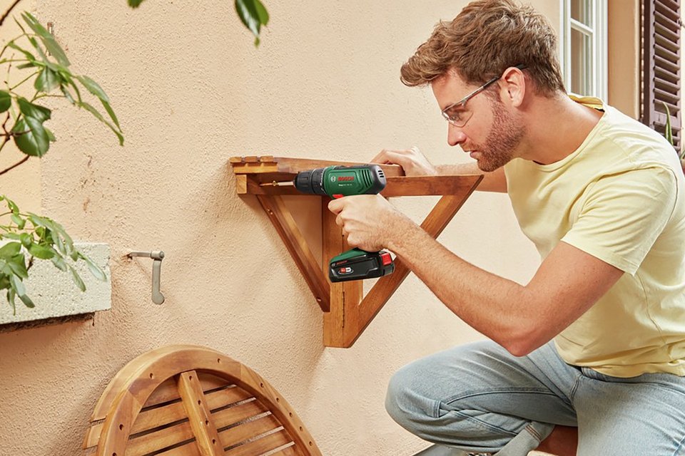 A man using Bosch EasyDrill 18V-40 Cordless Drill to put up a wall shelf.