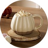 Cream shaped pumpkin mug placed onto a wooden coaster on an oak dining table.