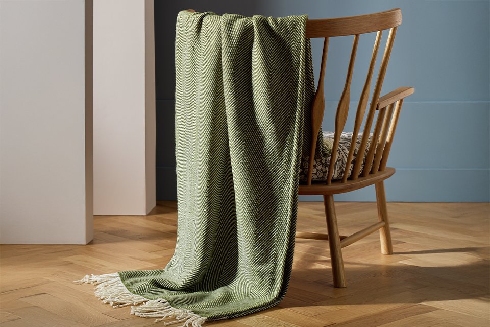 A Habitat herringbone throw in green on a wooden chair.