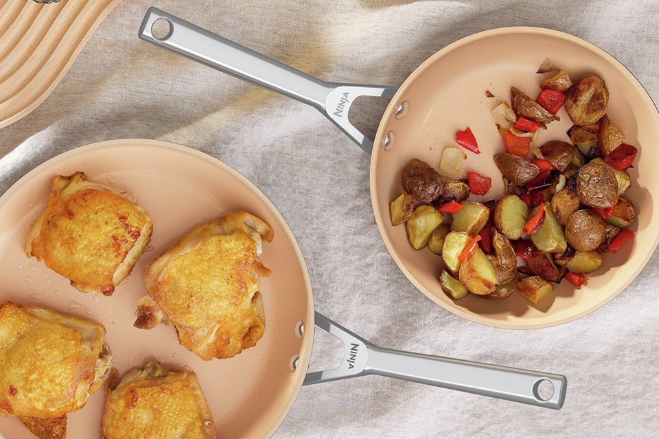 Ninja 28cm extended life ceramic aluminium woks with meat and potatoes cooked in them placed on a table.