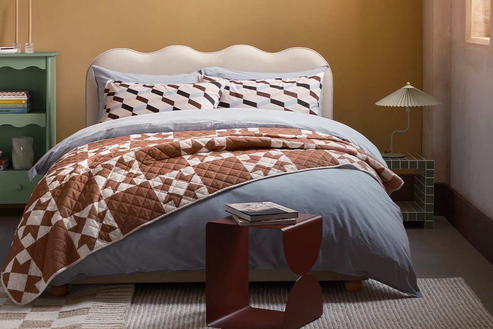 A bed made with Habitat patterned bedding and a lamp on a bedside table next to it.