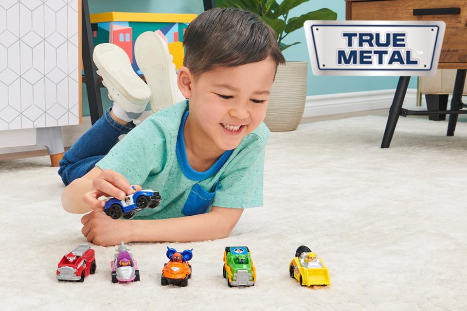 A boy playing with PAW Patrol True Metal die-cast vehicles, and the True Metal logo on top.