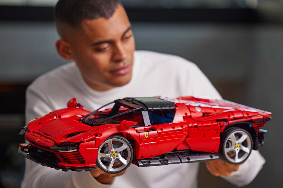 A young man holding a LEGO Technic Ferrari Daytona SP3 Model Race car set.