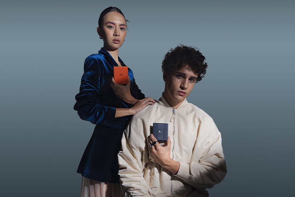 Stylish man and woman holding blue and orange motorola razr handsets. 