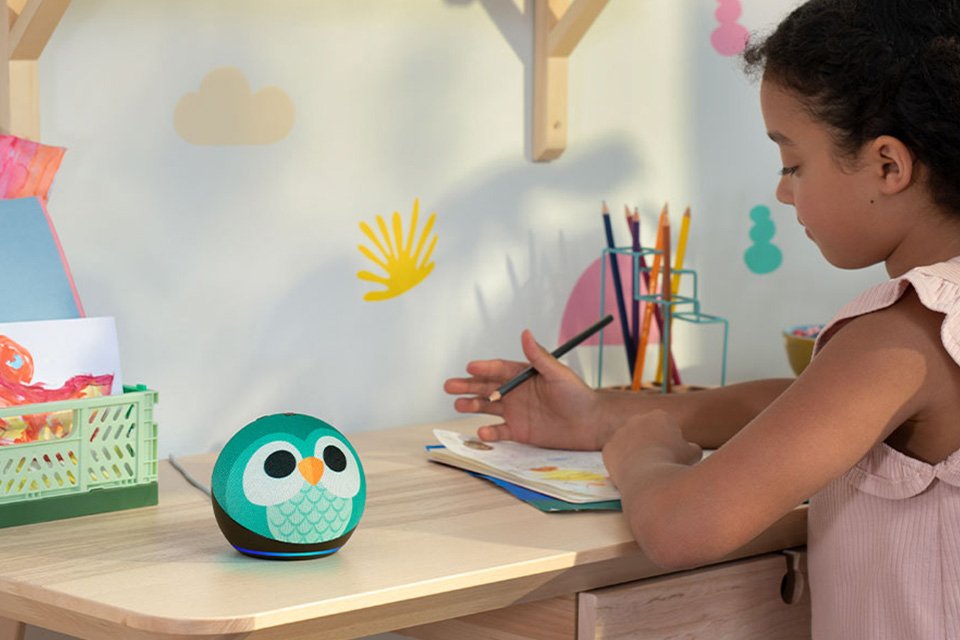 A girl doing her homework and an Amazon Echo Dot kids’ smart speaker in owl design is kept beside.