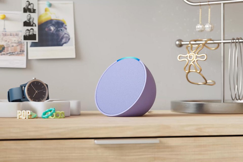 A purple Amazon Echo Pop smart speaker with Alexa placed on a dressing table with other things.