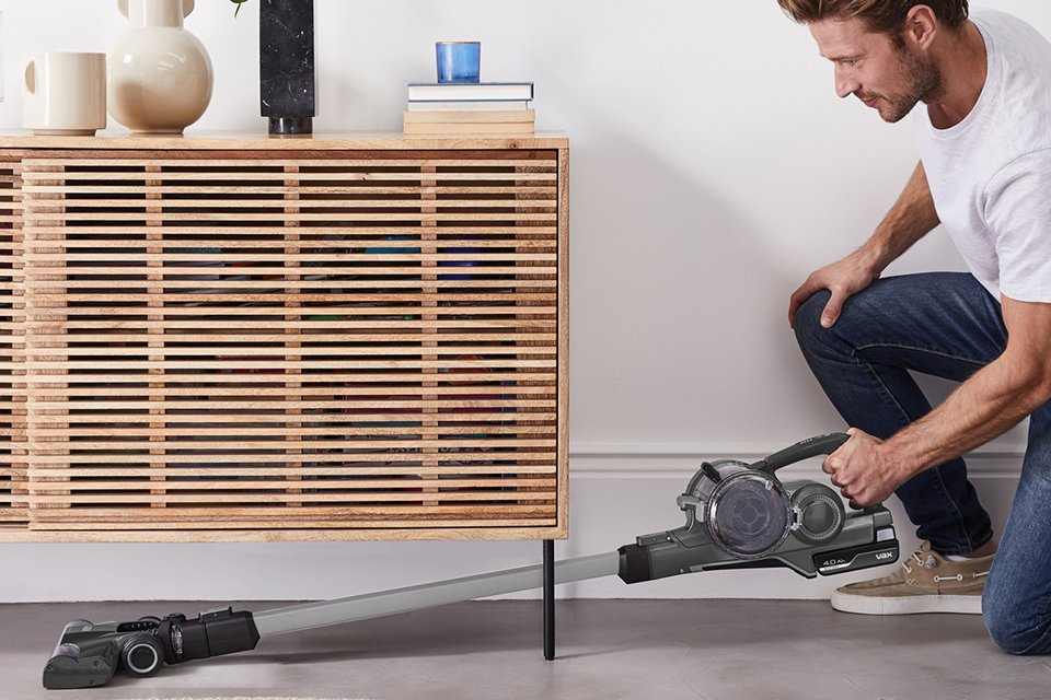 A man using Vax Blade 4 Classic Cordless Vacuum Cleaner to clean under a sideboard.