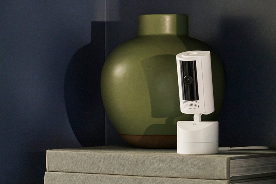 A Ring Pan tilt indoor camera placed on a table beside a green vase. 