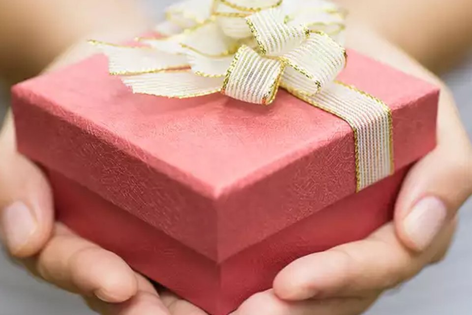 A person holding a gift box with a bow on top.