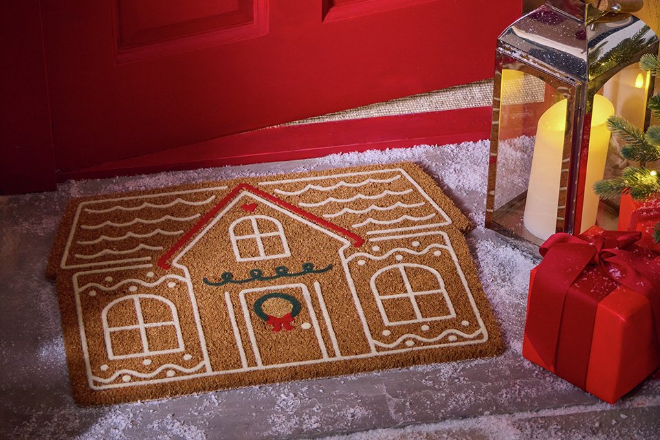 Gingerbread House Doormat near a candle outside a red door.