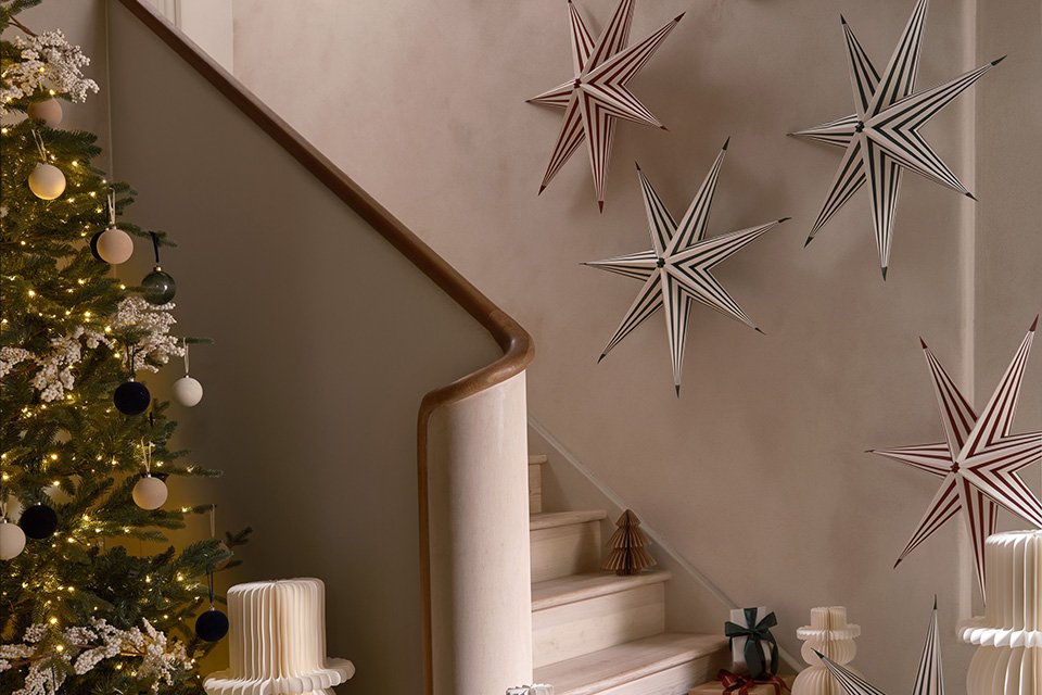 Christmassy decor like paper stars, snowman and gift boxes near a Christmas tree and a stairway.