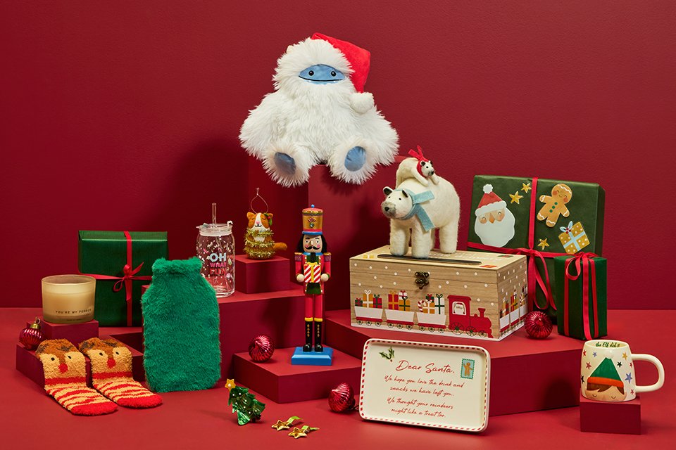 A wooden Christmas Eve box next to some Christmas ornaments, gift boxes, candles and a soft toy.