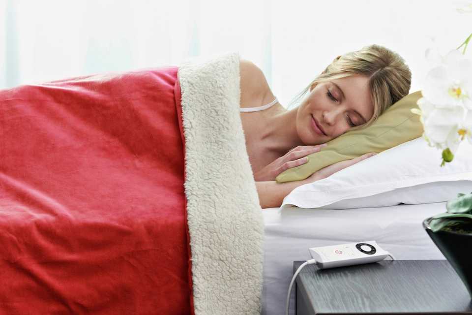 Woman sleeping on bed under red electric blanket.