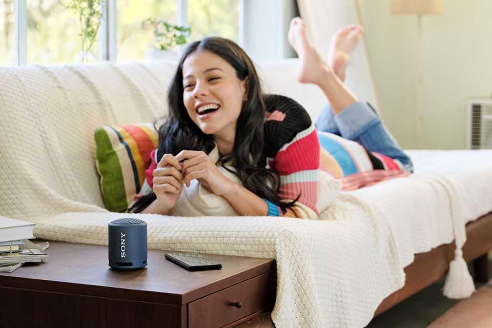 A woman lounging on sofa with Sony portable wireless speaker next to her.