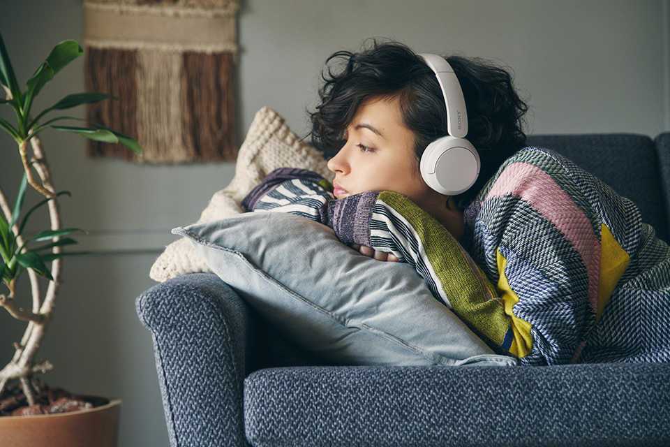 A woman lounging on the sofa with Sony wireless headphones on.