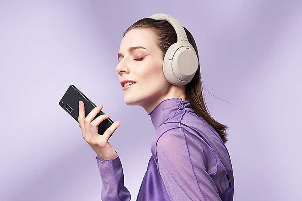 A woman with headphones on holding a Sony Xperia phone.