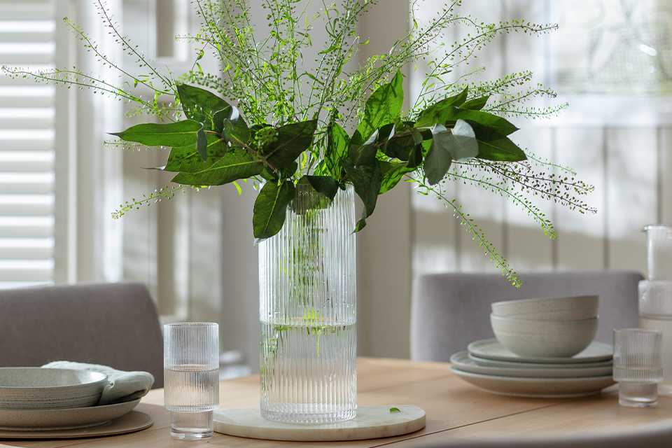Ribbed glass vase with foliage display on a dining table.