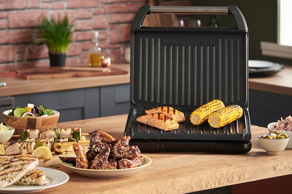 An open George Foreman grill with chicken and corn being grilled on it. 