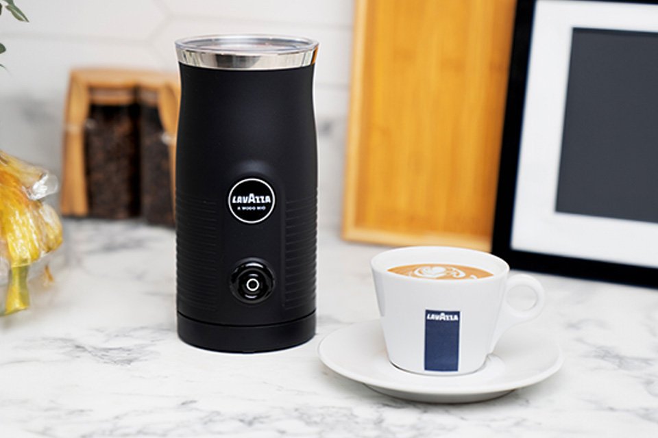 The black Lavazza Milk Easy frother placed next to a cup of cappuccino.