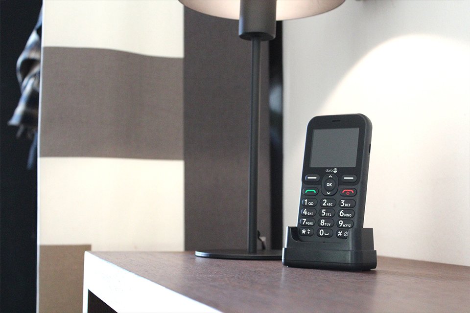 A black Doro Leva E10 feature phone placed in a charging cradle on a sideboard. 