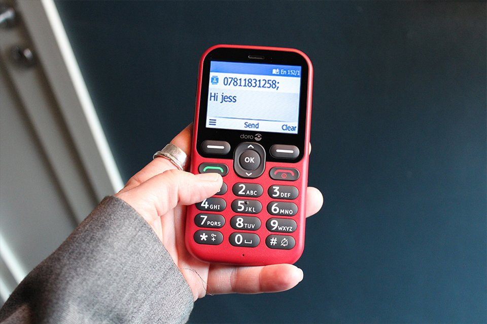 A lady holding a red Doro Leva E10 feature phone.