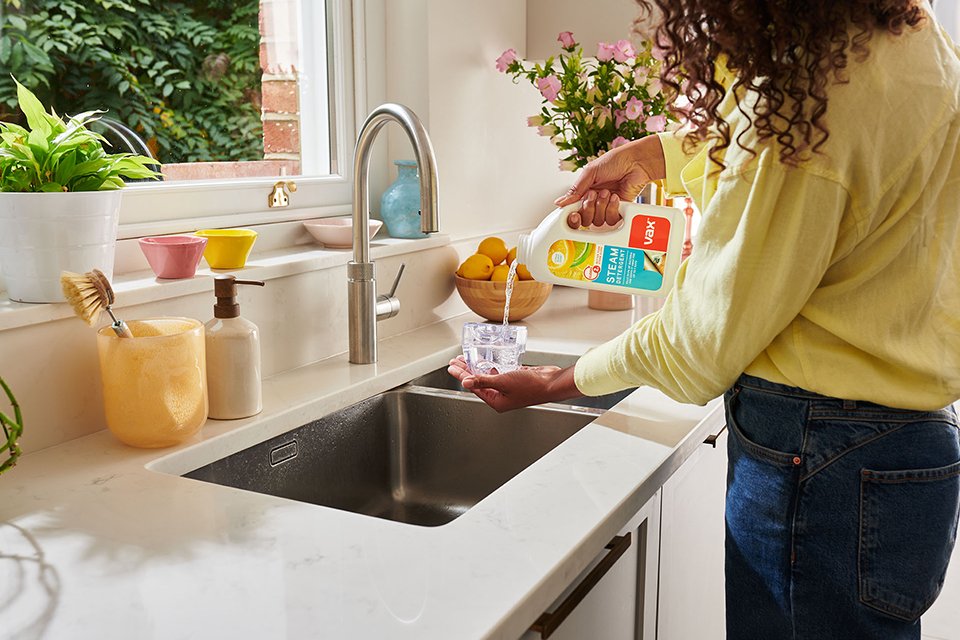 A woman pouring Vax solution in a cup over a sink.