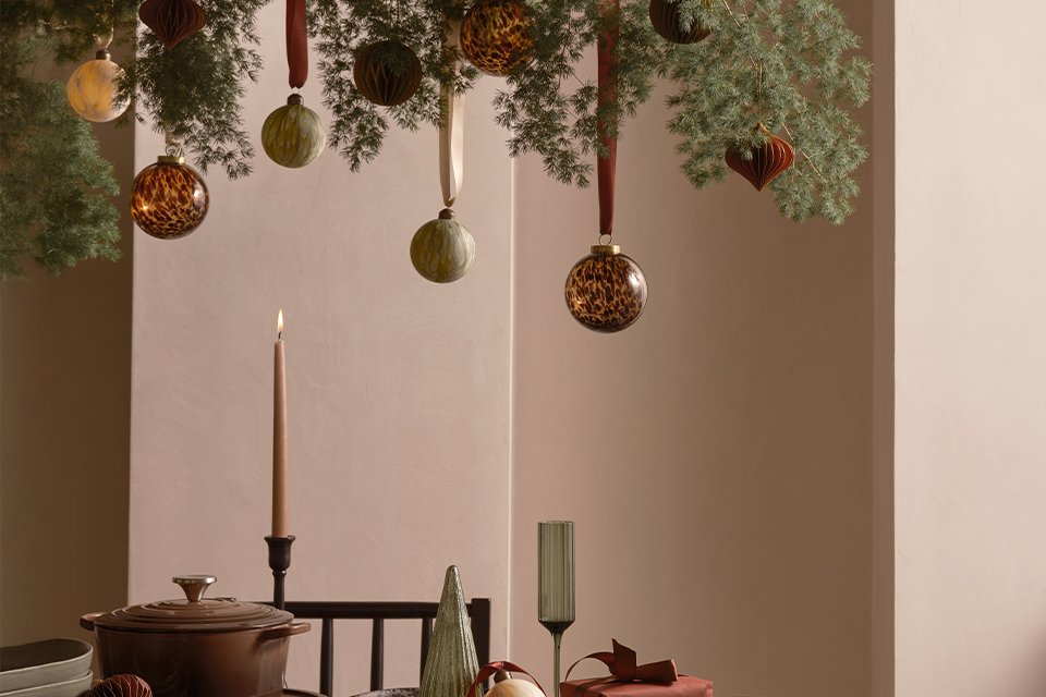 A table with glasses, plates and serveware and Christmas decorations hanging on top.