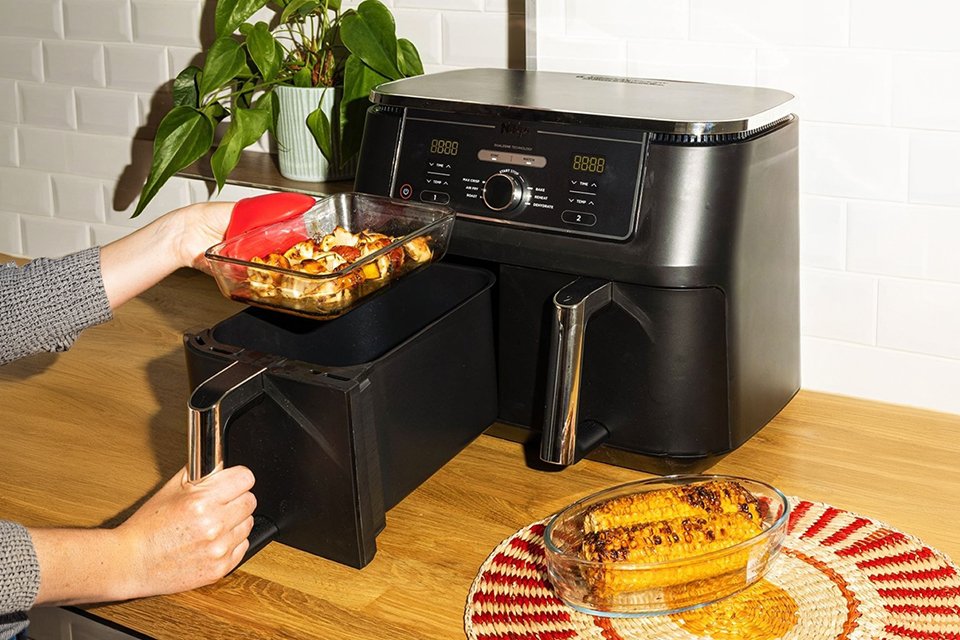 A person placing a Pyrex rectangular glass air fryer dish with chicken in it into an air fryer.