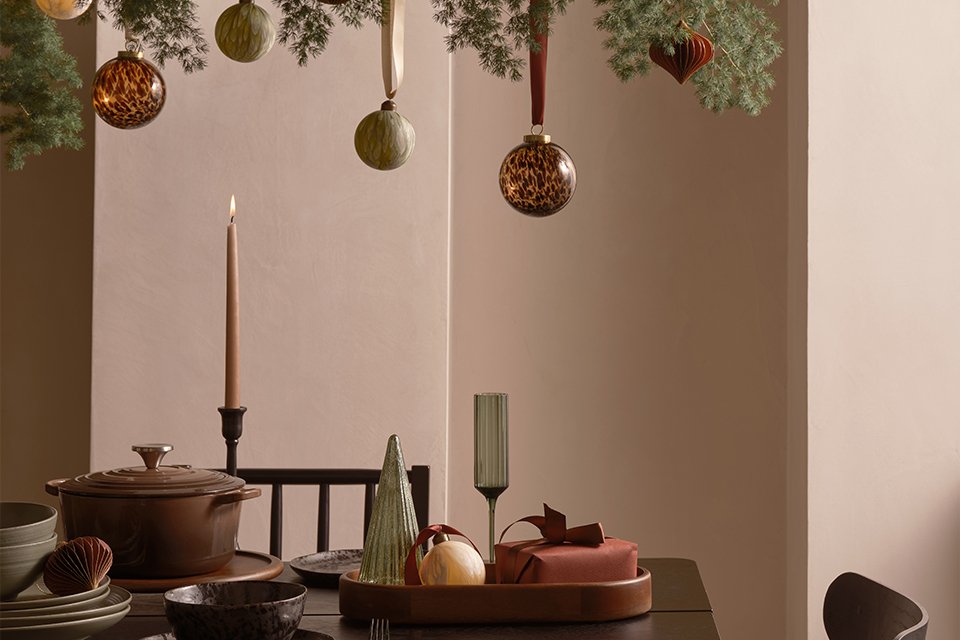 A table set up for hosting with baubles and Christmas decorations as well as stylish tableware and glasses.