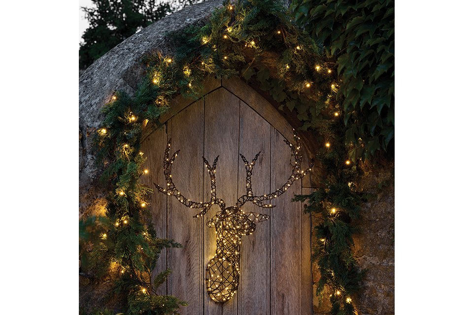 Light up stag head hanging on an outside gate surrounded by a garland with lights 
