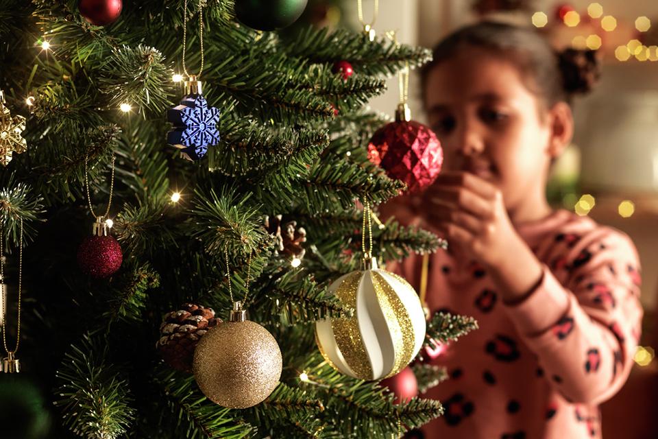 A small girl hanging baubles on a Christmas tree.