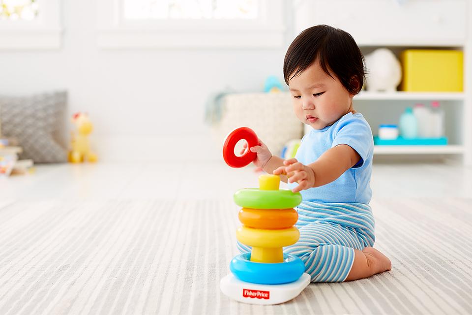 Deep in concentration, a baby puts the final piece atop a Fisher-Price stacking toy.