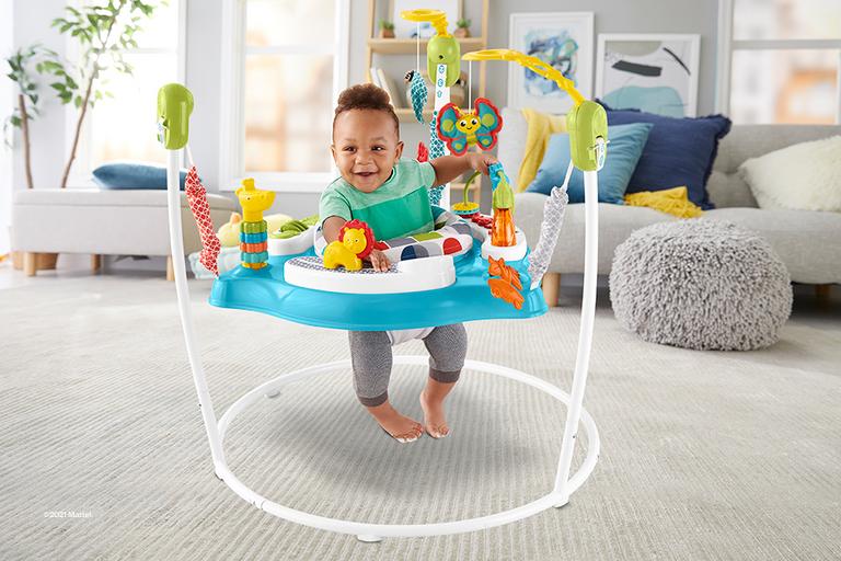A smiling baby bounces up and down in a colourful baby bouncer/gym combo.