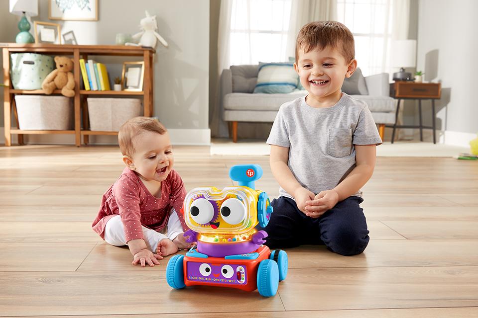 A toddler and a baby are both smiling at a chunky Fisher-Price robot toy.