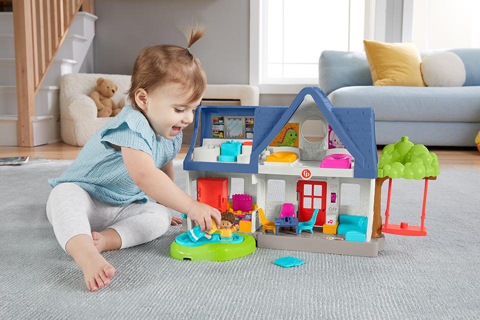 A baby plays with a colourful Fisher-Price toy house.
