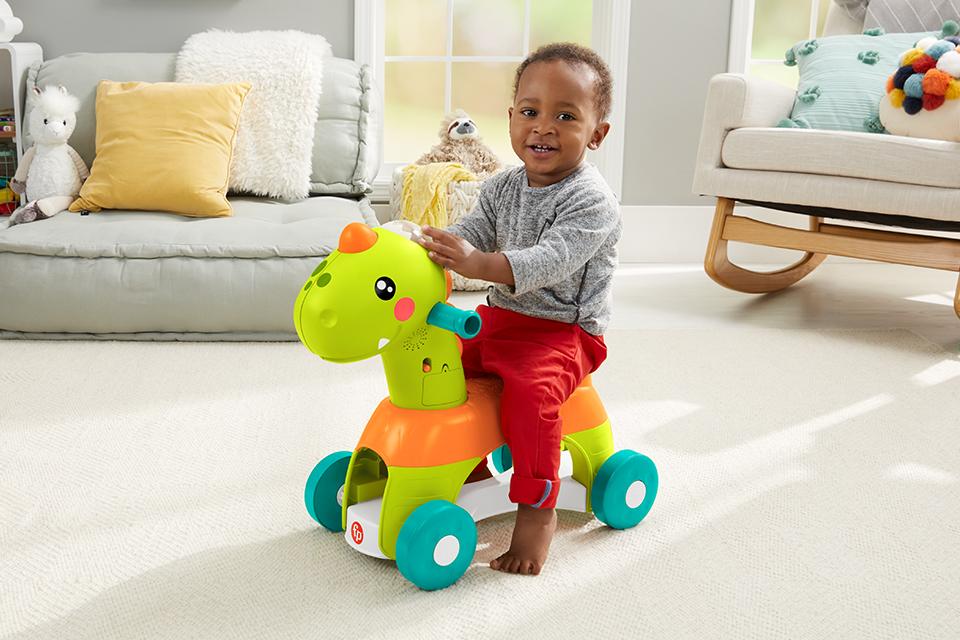 A toddler rides a Fisher-Price Rool and Roar Dino across a soft cream carpet.