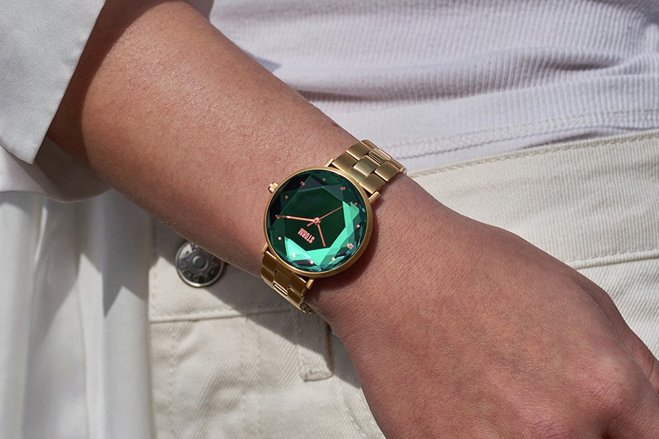A woman wearing a STORM Elexi green dial stainless steel strap watch and a gold ring band on her right hand.