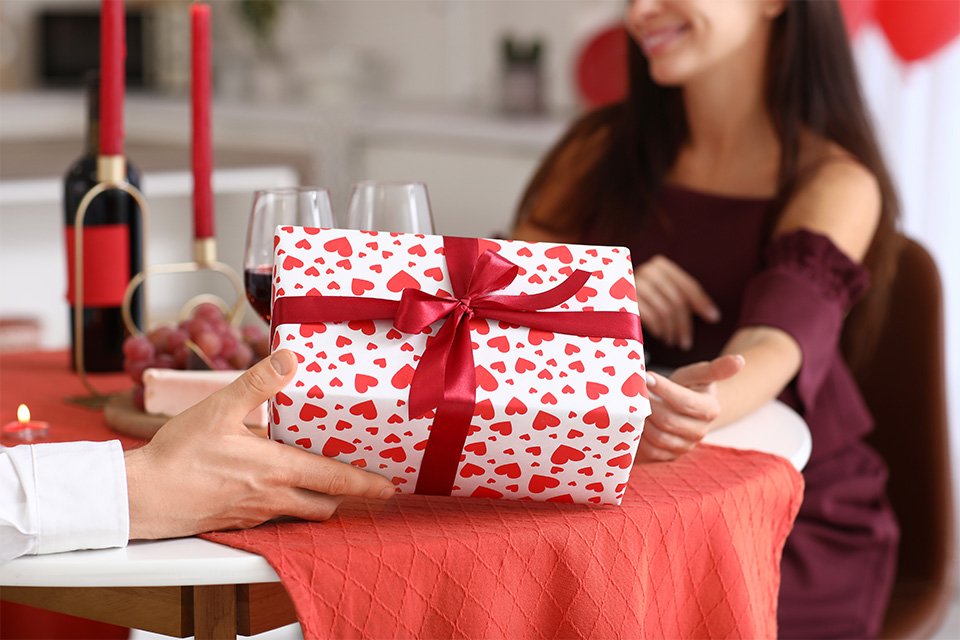 A husband giving an anniversay gift wrapped in a white and red wrapping paper to his wife.