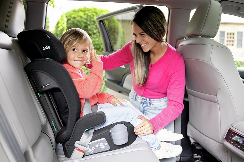 A mother looking at her child secured in a Joie Elevate R129 Toddler to Booster Car Seat - Shale.