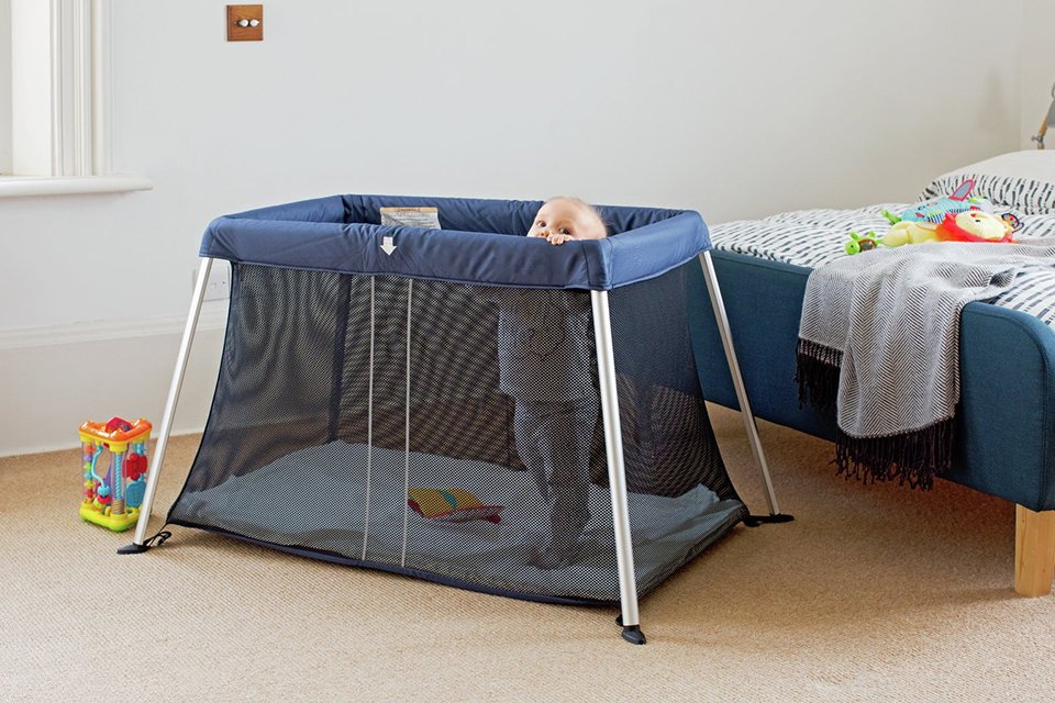 A baby in a Cuggl Deluxe Superlight Travel Cot.