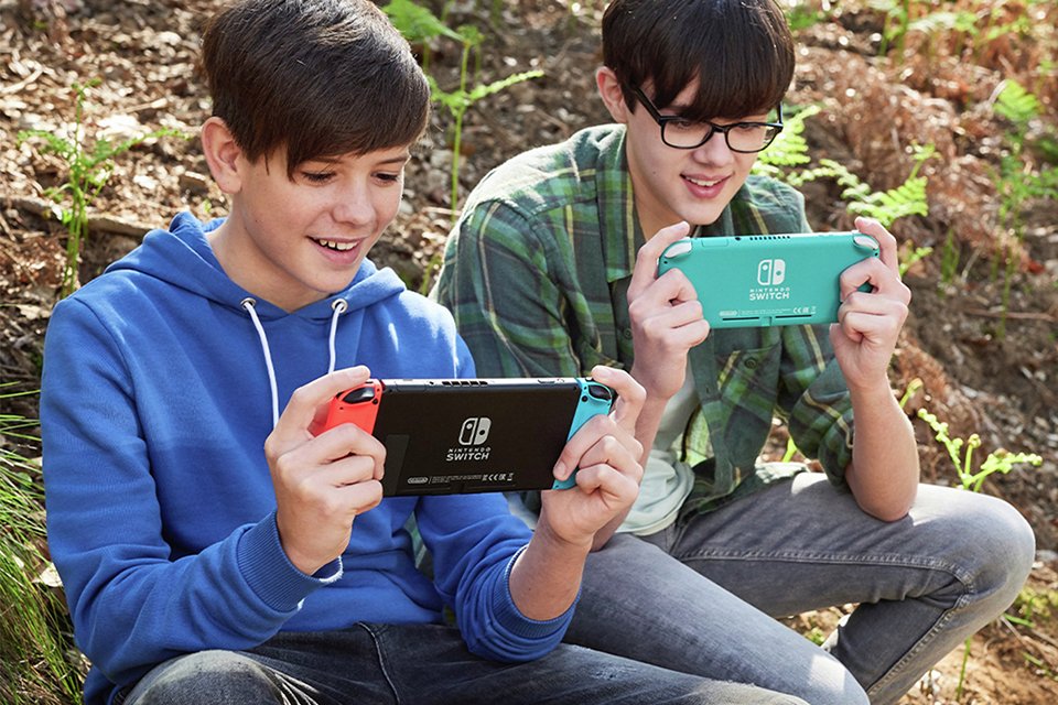 Two boys playing on Nintendo Switch consoles outdoors. 