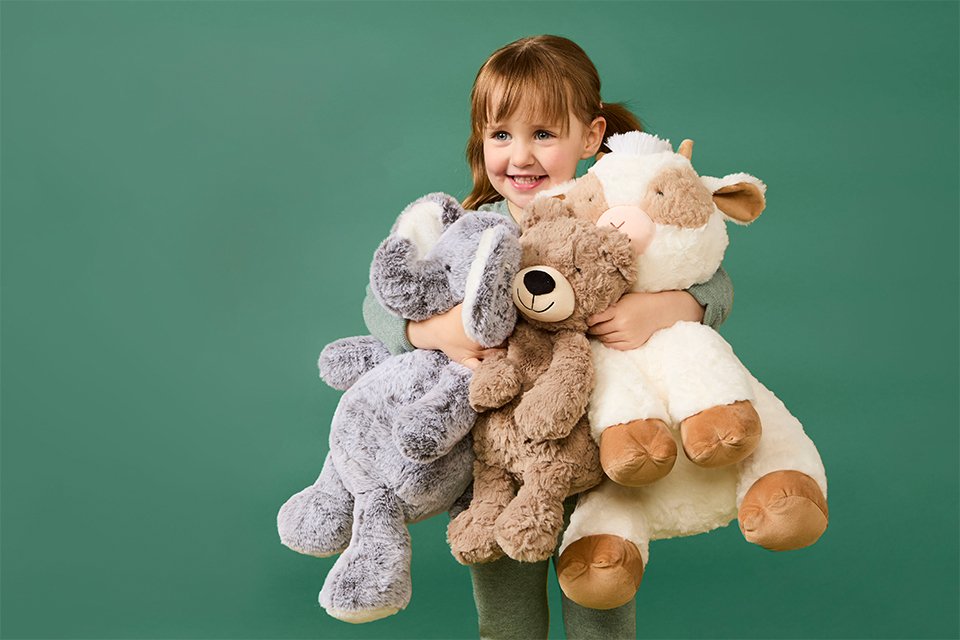 A girl holding multiple plush toys close to her while smiling at the camera.