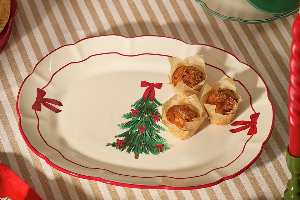 A serving plate with bows on the sides and a Christmas tree motif placed on a striped tablecloth.